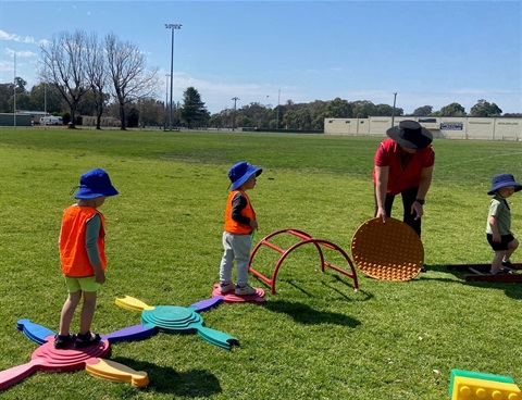 Young children participating in an obstacle course set up on the grass.